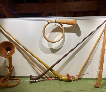 Eine Sammlung traditioneller Holzblasinstrumente ist an einer Wand ausgestellt, darunter Hörner und Schalmeien.