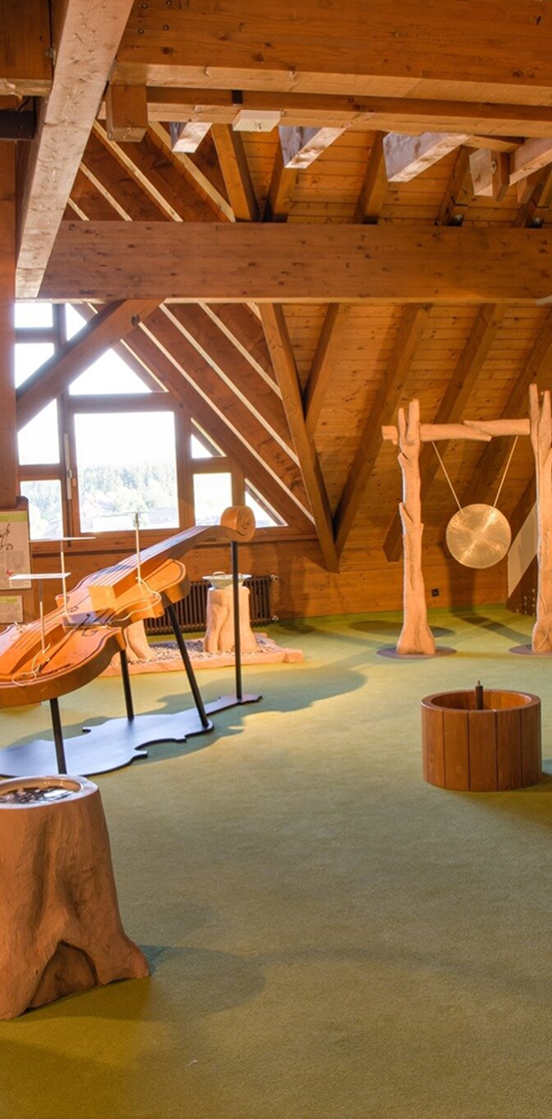 Holzverkleideter Raum mit interaktiven Stationen, darunter ein großes Musikinstrument und eine Klanginstallation.