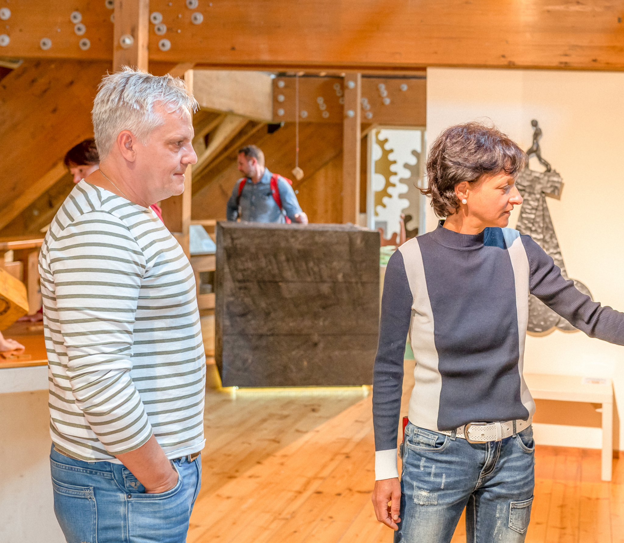 Zwei Menschen in einer Galerie betrachten Kunstwerke. Im Hintergrund sind weitere Besucher zu sehen.