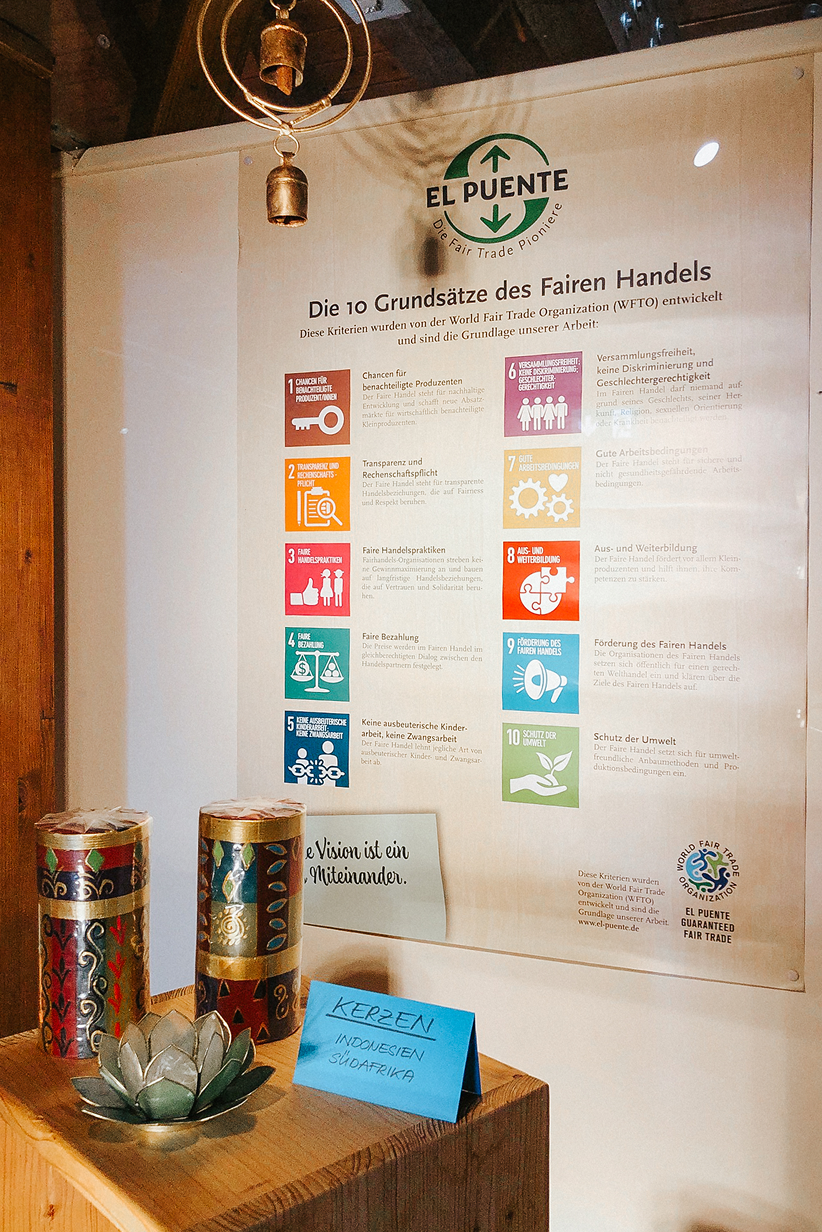 Ein Informationsblatt zu Fair Trade Prinzipien mit Kerzen und Dekoration aus Holz in einem Ausstellungsraum.
